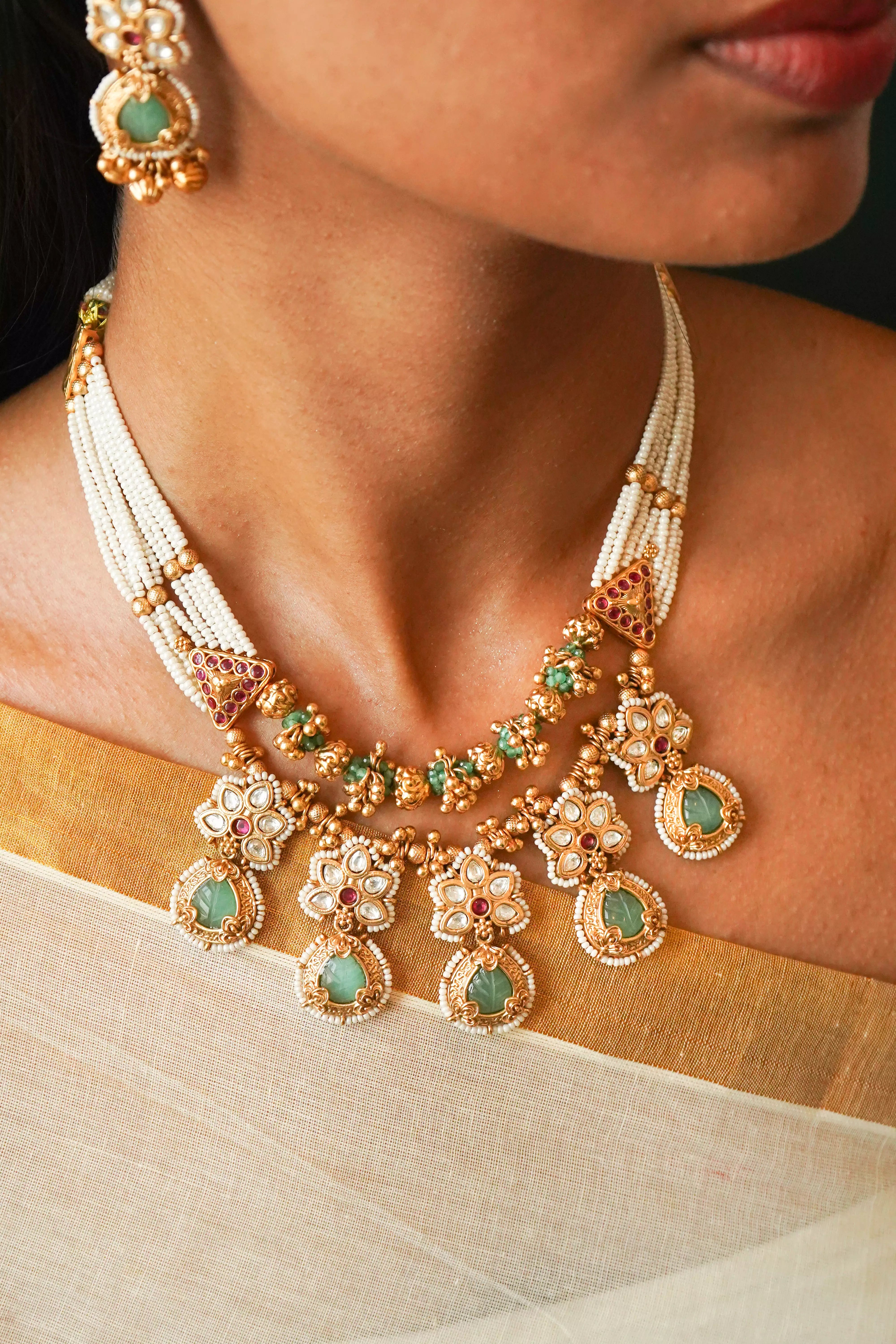 Close-up of a woman wearing an ornate necklace with green gemstones and gold accents.