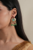 Close-up of a woman wearing a gold earring with green and red stones against a neutral background